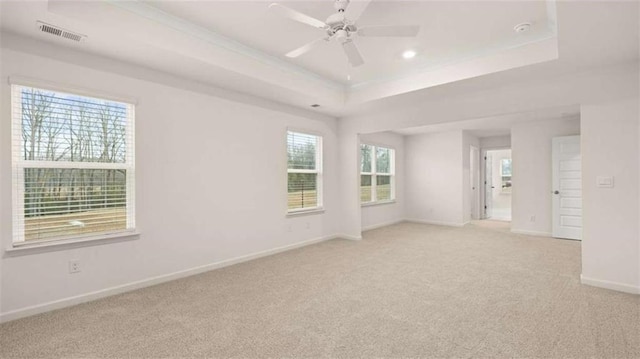 empty room with a raised ceiling, light colored carpet, visible vents, ceiling fan, and baseboards