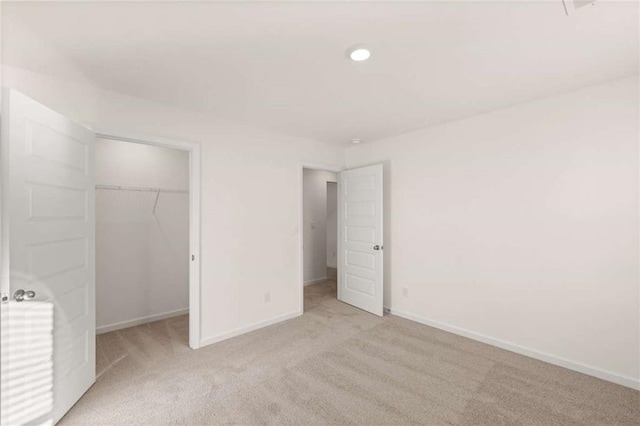 unfurnished bedroom with a closet, light colored carpet, a spacious closet, and baseboards