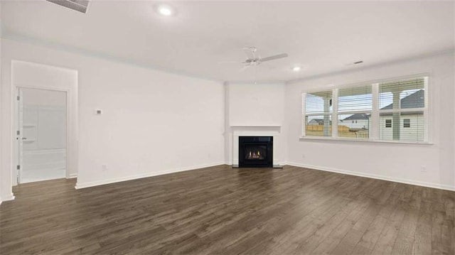 unfurnished living room featuring a warm lit fireplace, visible vents, baseboards, a ceiling fan, and dark wood-type flooring