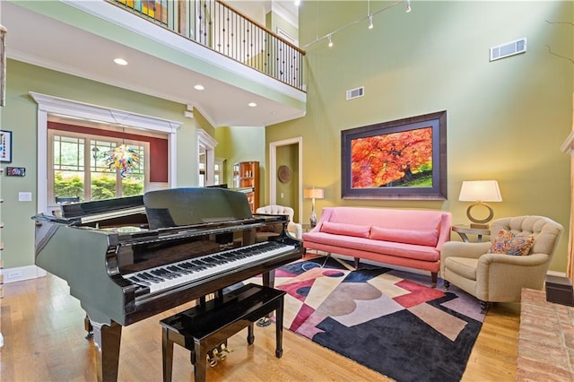 sitting room featuring crown molding, a towering ceiling, wood finished floors, and visible vents