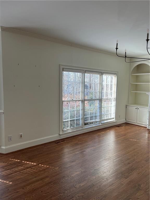 empty room featuring built in shelves, ornamental molding, and dark hardwood / wood-style flooring