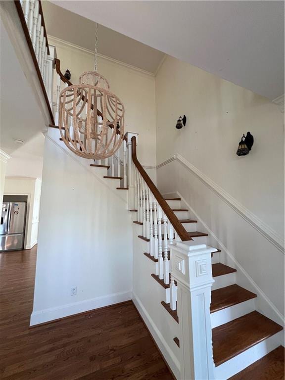 staircase with crown molding, hardwood / wood-style floors, and an inviting chandelier