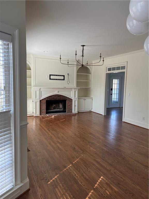 unfurnished living room with crown molding, a brick fireplace, dark hardwood / wood-style flooring, and built in shelves