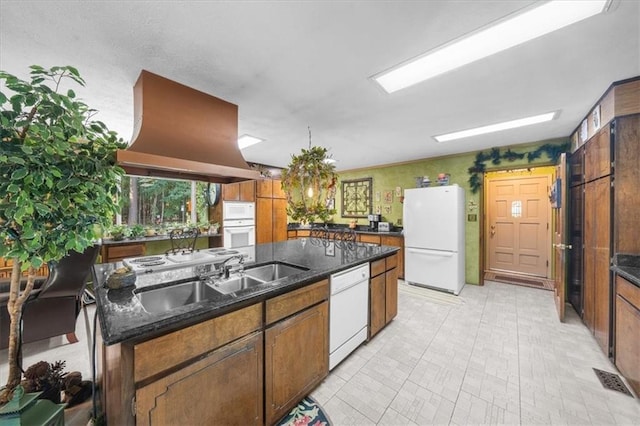 kitchen with dark stone counters, a kitchen island with sink, sink, white appliances, and exhaust hood