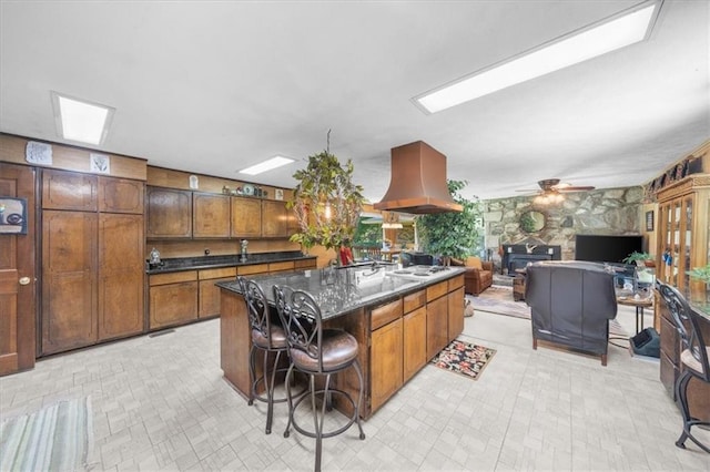 kitchen with a breakfast bar, white gas cooktop, ventilation hood, a center island with sink, and ceiling fan