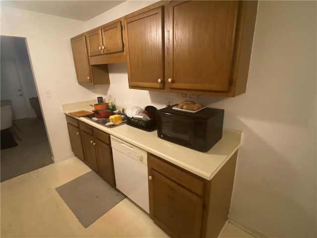 kitchen with brown cabinetry, black microwave, baseboards, dishwasher, and light countertops