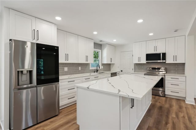 kitchen with light stone countertops, a center island, sink, white cabinets, and appliances with stainless steel finishes