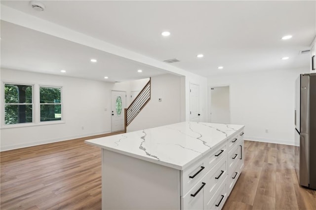 kitchen with white cabinets, light hardwood / wood-style floors, a kitchen island, light stone counters, and stainless steel refrigerator