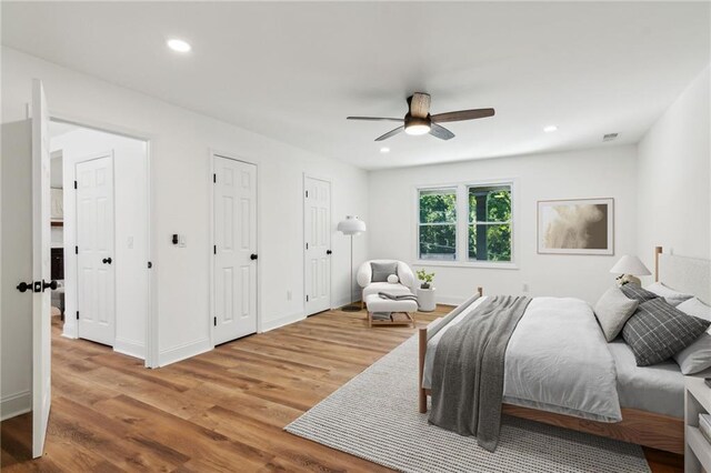 bedroom with hardwood / wood-style flooring, ceiling fan, and multiple closets