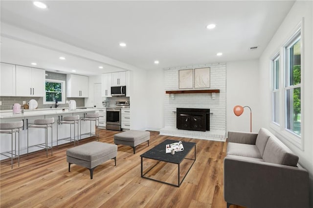 living room with a fireplace, light wood-type flooring, a healthy amount of sunlight, and sink