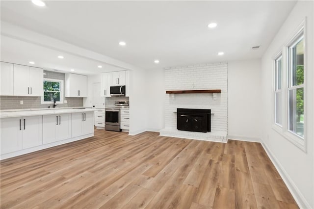 kitchen featuring a fireplace, white cabinets, stainless steel appliances, and light hardwood / wood-style flooring