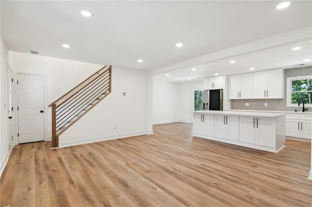 kitchen with sink, stainless steel refrigerator with ice dispenser, tasteful backsplash, a kitchen island, and white cabinetry