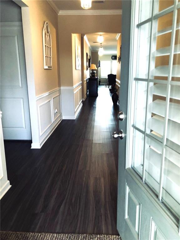 hall featuring dark wood-type flooring, ornamental molding, wainscoting, and a decorative wall