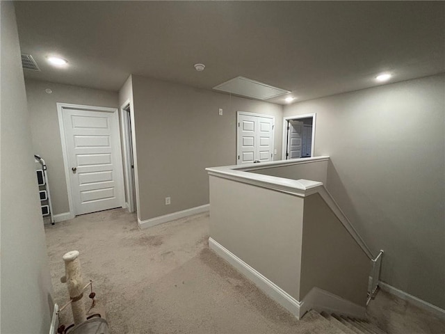 corridor featuring visible vents, an upstairs landing, baseboards, light colored carpet, and attic access