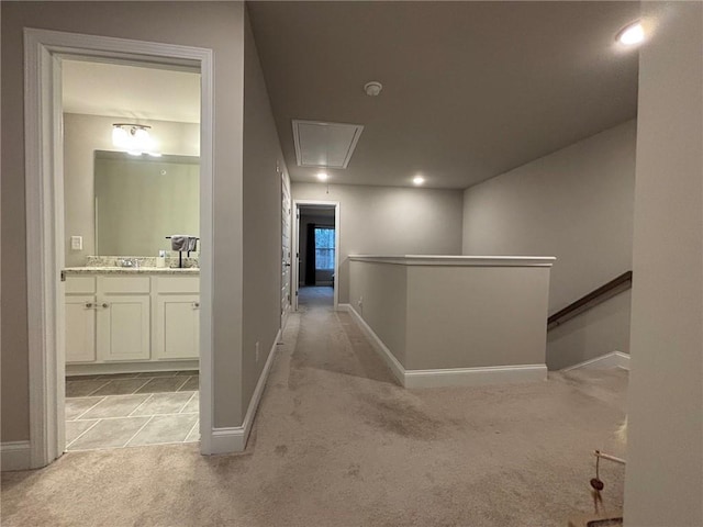 corridor with an upstairs landing, light colored carpet, attic access, and baseboards