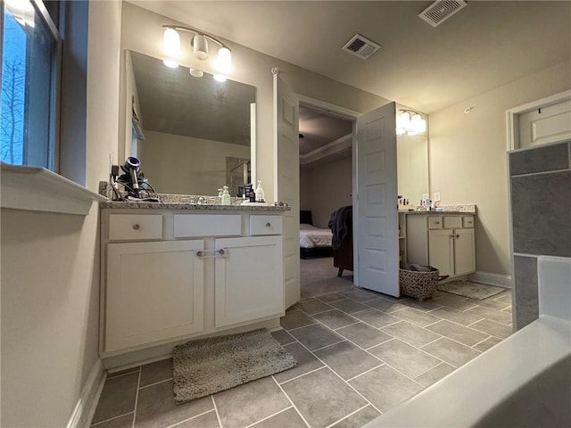 full bath with visible vents, baseboards, two vanities, and ensuite bath