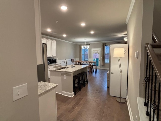 kitchen featuring dark wood-type flooring, an island with sink, a sink, white cabinetry, and crown molding