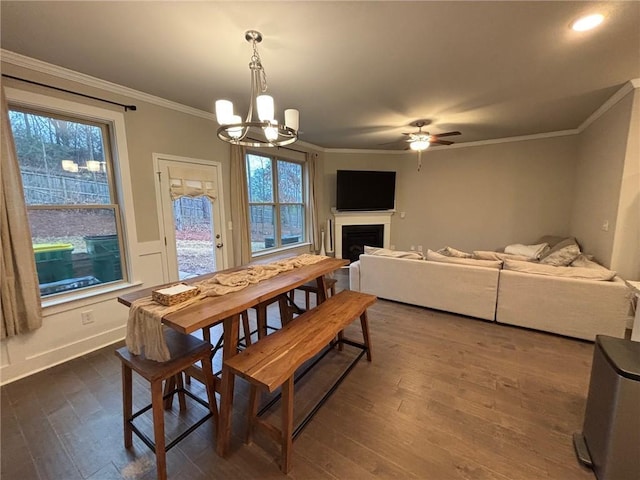 dining room with baseboards, dark wood finished floors, a fireplace, ornamental molding, and ceiling fan with notable chandelier