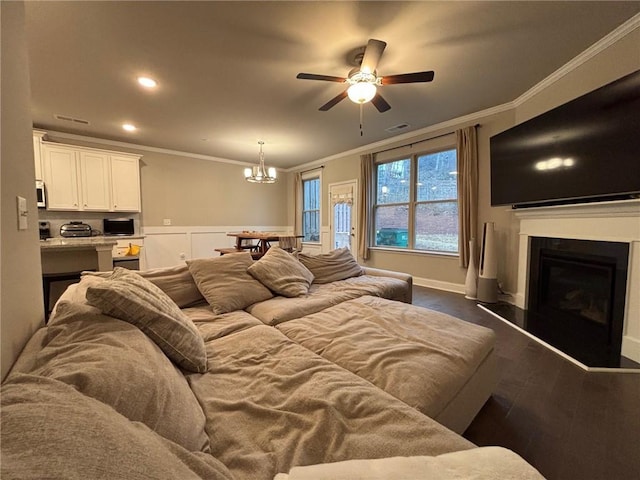 living area with visible vents, dark wood-type flooring, a fireplace with raised hearth, ceiling fan with notable chandelier, and crown molding