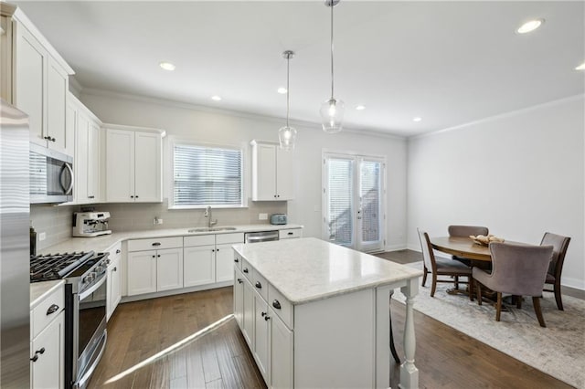 kitchen with hanging light fixtures, a kitchen island, white cabinets, appliances with stainless steel finishes, and sink