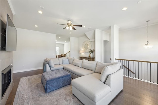 living room featuring a tiled fireplace, dark wood-type flooring, crown molding, and ceiling fan