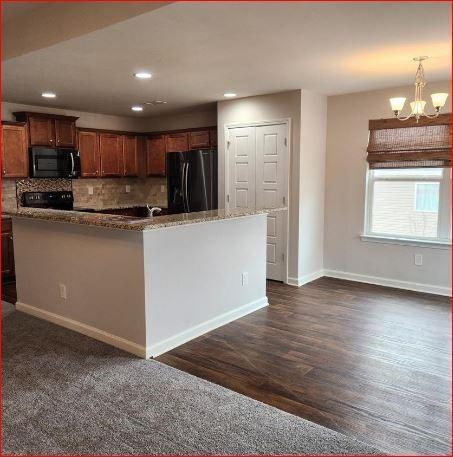 kitchen featuring pendant lighting, backsplash, black fridge, dark hardwood / wood-style flooring, and a chandelier