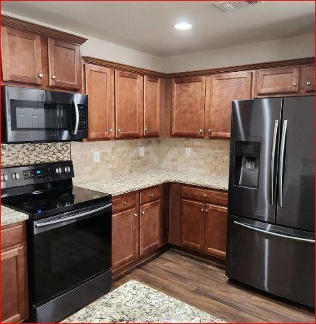 kitchen featuring stainless steel appliances, light stone countertops, dark wood-type flooring, and decorative backsplash