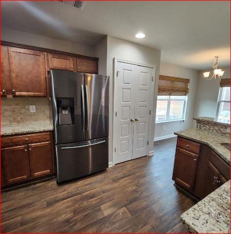 kitchen featuring dark wood-type flooring, decorative backsplash, light stone counters, and stainless steel fridge with ice dispenser