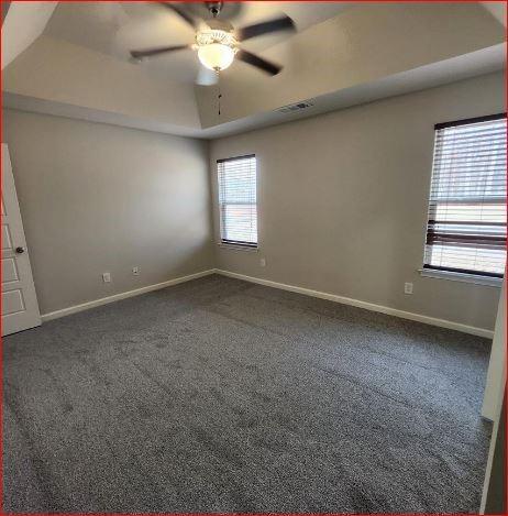 unfurnished room with ceiling fan, a tray ceiling, and dark colored carpet