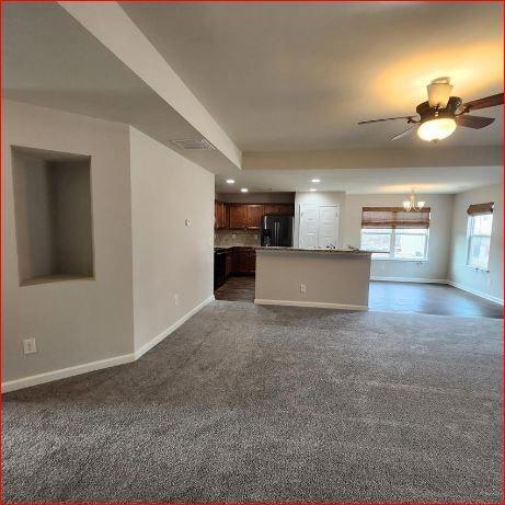 unfurnished living room with dark carpet and ceiling fan with notable chandelier