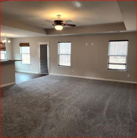 spare room with ceiling fan with notable chandelier, a tray ceiling, and dark carpet