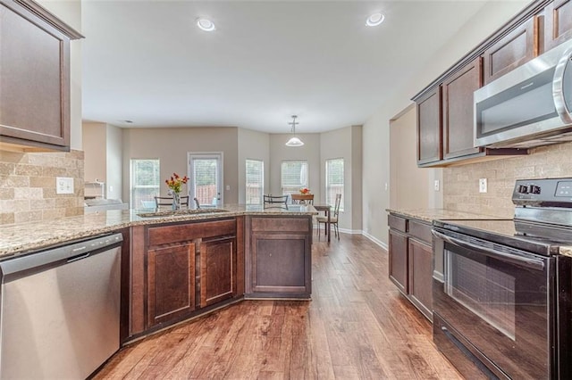 kitchen with appliances with stainless steel finishes, healthy amount of natural light, light wood-type flooring, light stone countertops, and recessed lighting