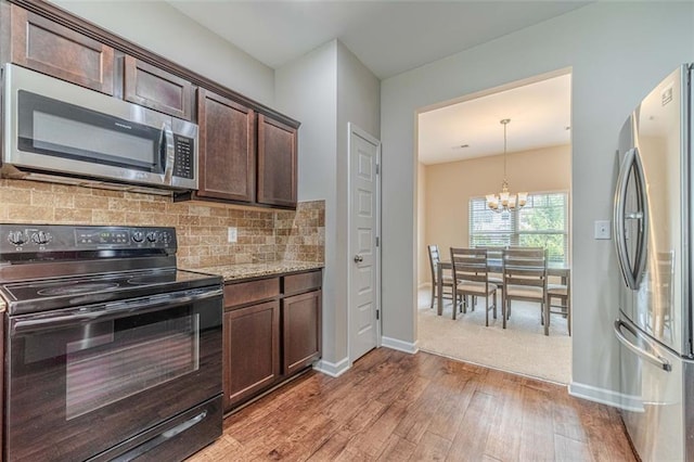 kitchen with stainless steel appliances, light wood-style flooring, a chandelier, dark brown cabinets, and backsplash