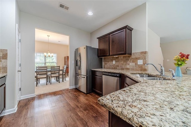 kitchen with appliances with stainless steel finishes, dark wood-type flooring, dark brown cabinets, a chandelier, and light stone counters