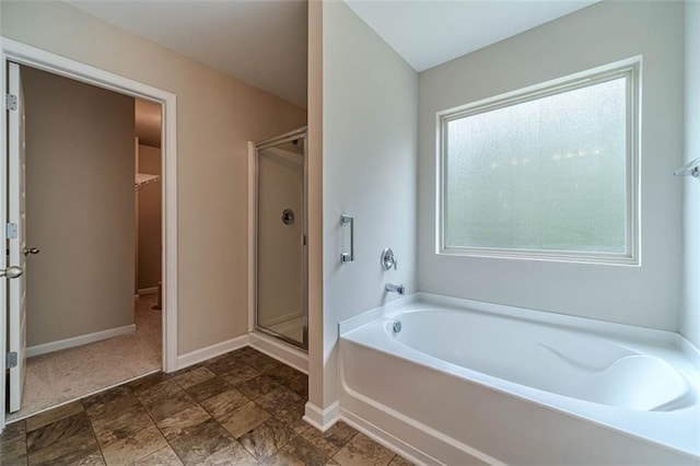 full bath featuring a garden tub, a shower stall, a walk in closet, and stone finish floors