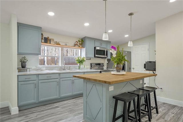 kitchen with a kitchen island, sink, hanging light fixtures, appliances with stainless steel finishes, and butcher block counters