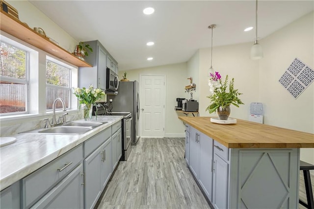 kitchen with a breakfast bar area, stainless steel appliances, hanging light fixtures, vaulted ceiling, and sink