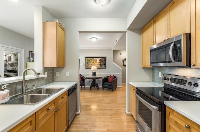 kitchen featuring stainless steel appliances, a sink, light countertops, backsplash, and light wood finished floors