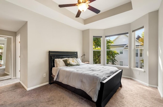 bedroom featuring light carpet, baseboards, a raised ceiling, and a ceiling fan