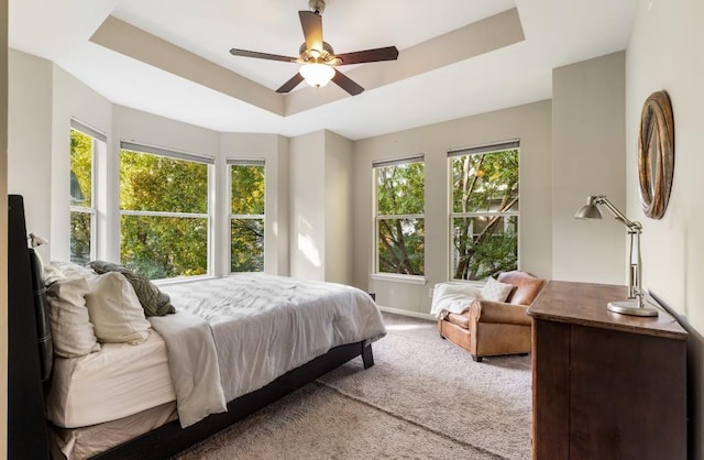 carpeted bedroom with ceiling fan, a raised ceiling, and baseboards