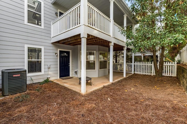 view of exterior entry with central AC, a patio, fence, and a balcony