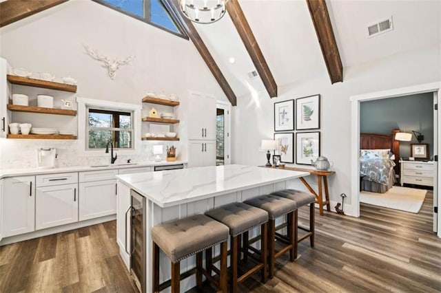 kitchen featuring visible vents, white cabinets, beamed ceiling, open shelves, and a sink