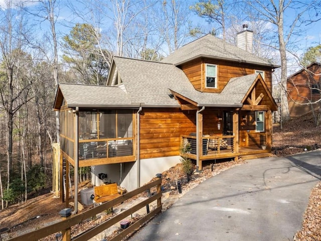 chalet / cabin with a sunroom, a chimney, and roof with shingles