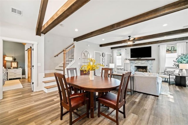 dining area with ceiling fan, a fireplace, visible vents, stairs, and light wood-type flooring