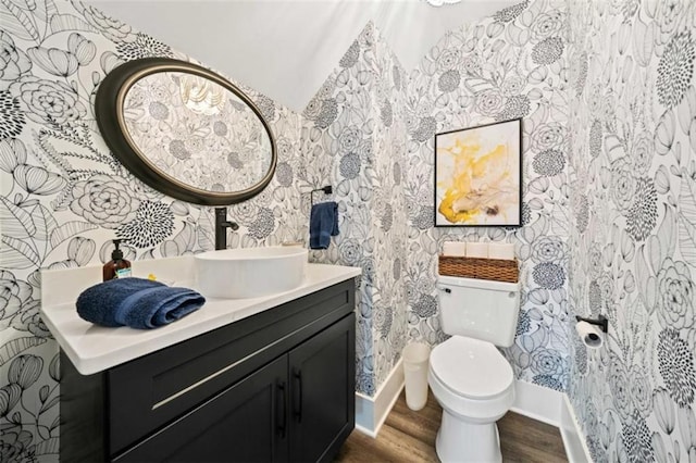 bathroom featuring toilet, wood finished floors, vanity, baseboards, and wallpapered walls