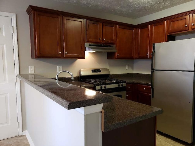 kitchen with dark stone counters, appliances with stainless steel finishes, a peninsula, a textured ceiling, and under cabinet range hood