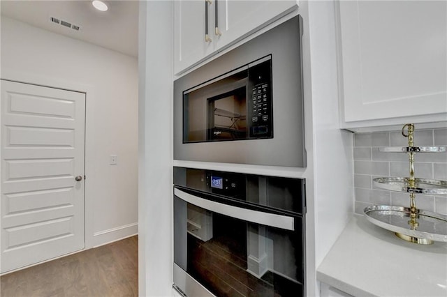 8305 Beryl Overlook, Gainesville, GA 30506 - kitchen view of oven, white cabinetry, tasteful backsplash, stainless steel microwave, and wood finished floors