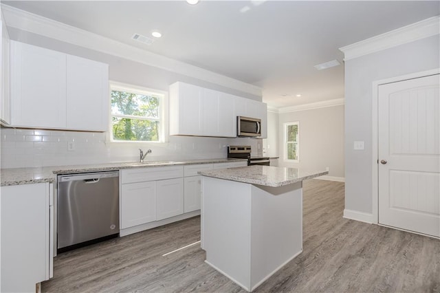 kitchen featuring light wood finished floors, stainless steel appliances, ornamental molding, and tasteful backsplash
