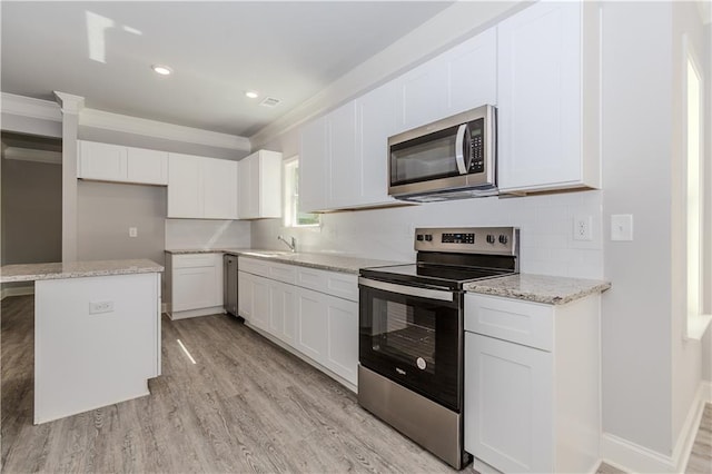 kitchen featuring light wood finished floors, decorative backsplash, stainless steel appliances, and a sink