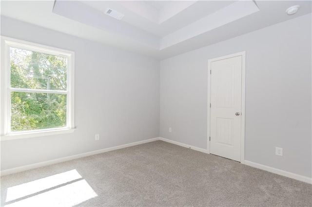 spare room featuring carpet floors, baseboards, visible vents, and a raised ceiling